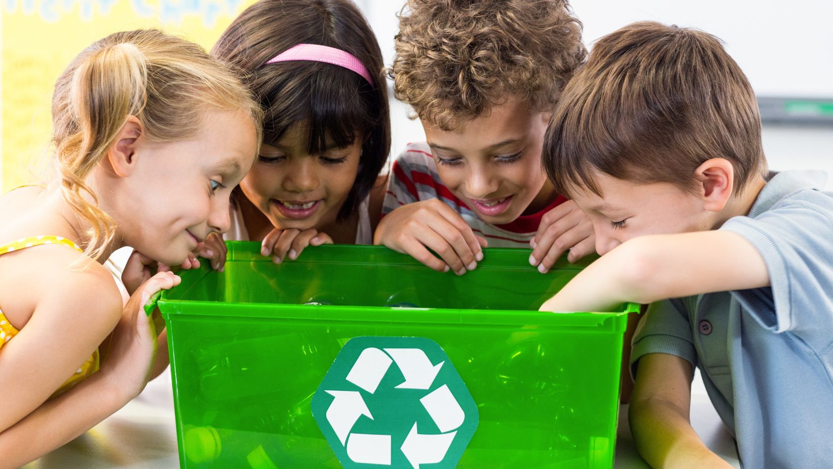 a group of children looking at a green recycle bin