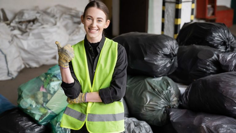 A worker in front of a pile of garbage bags